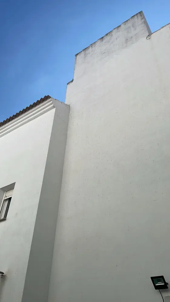 Parte alta de una fachada blanca con manchas de guano de murciélago bajo el remate y las tejas